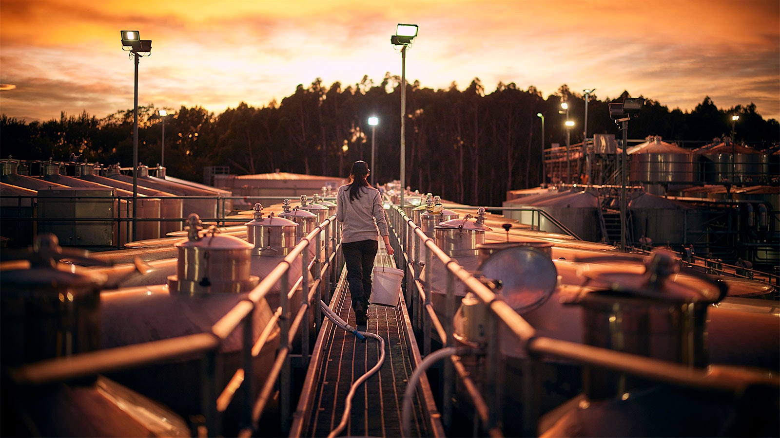 A worker walks among outdoor stainless-steel tanks at sundown.